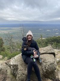 Portrait of man sitting on rock against sky