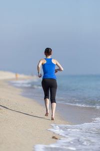 Full length of woman walking on beach against clear sky