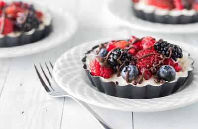 Small mixed berry cheesecake tarts drizzled with chocolate, ready for eating.