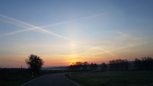 Road amidst trees against sky during sunset