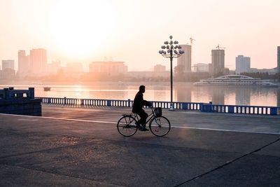 Man riding bicycle on bridge against buildings in city