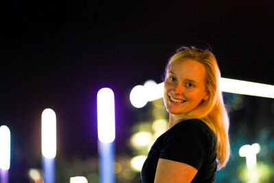 Close-up portrait of smiling young woman standing against sky at night