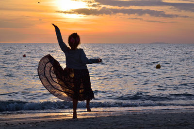 Rear view of silhouette girl jumping on beach against sky