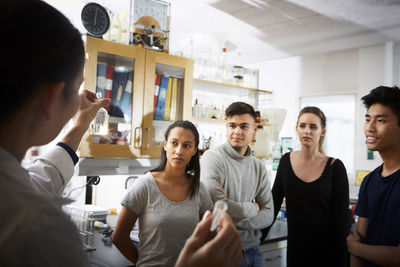 Rear view of mature female teacher showing solution while explaining to young multi-ethnic students in laboratory