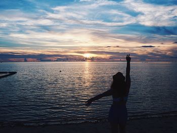 Rear view of silhouette woman standing at beach during sunset