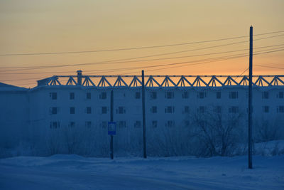 Bridge over snow covered buildings against sky during sunset