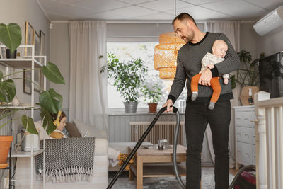 Father carrying baby while vacuum cleaning