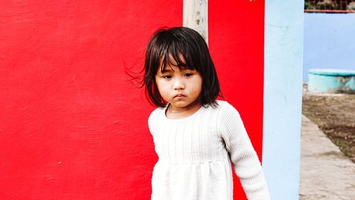 Portrait of cute girl standing against red wall