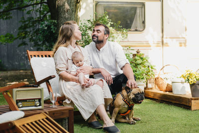 Family with baby and dog spending happy time together near trailer outside on deck chair, traveling