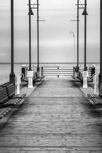 Empty wooden boardwalk,  view out to the horizon, no people, seagulls line the rail. black and white