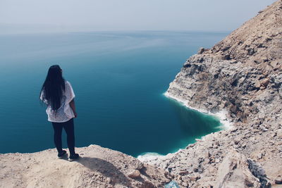 Rear view of girl standing on cliff by the sea