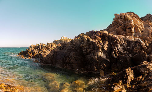 Rock formations by sea against clear sky