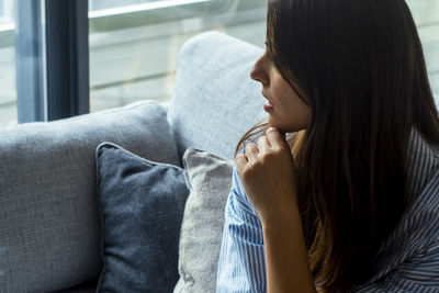 Side view of young woman sitting on sofa at home