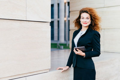 Young woman using phone while standing on wall