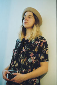 Young woman with eyes closed standing against wall