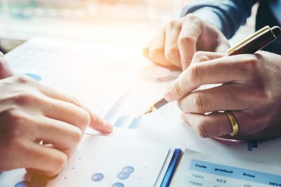 Cropped hands of colleagues discussing graphs in meeting at office