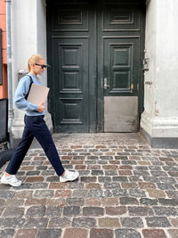 Woman wearing sunglasses going to work holding magazine against the green wall and the city