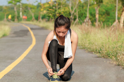 Young woman tying shoelace on road