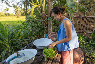 Side view of woman standing by plants in yard