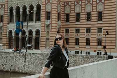 Young woman wearing sunglasses standing against buildings in city