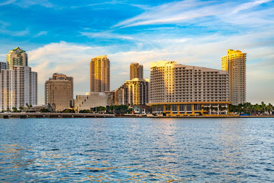 Buildings by river against sky in city