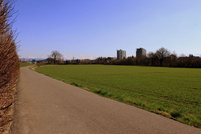 Scenic view of field by buildings against clear sky