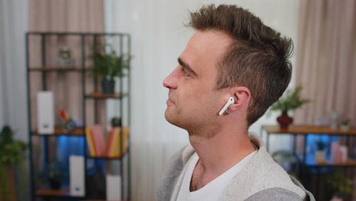 Young man wearing earphone looking away at home