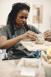 Mature woman molding clay sitting at table in art class