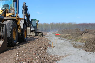 Bulldozers on field against blue sky