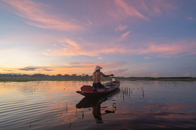 Man sitting in boat on lake against sky during sunset