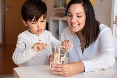 Mother assisting son in puzzle sitting at home