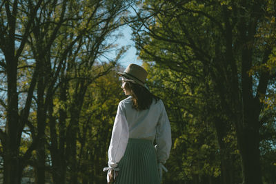 Rear view of woman standing against trees at park