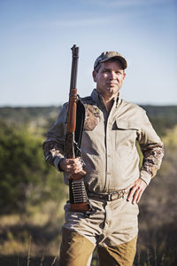 Portrait of hunter holding rifle while standing against sky