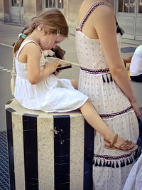 Girl using phone while sitting by mother in city