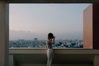 Woman standing on balcony against buildings in city