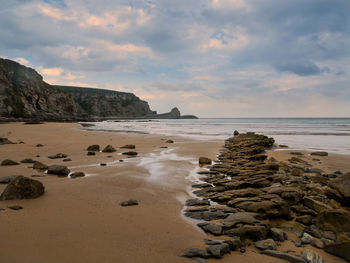 Rocks on beach against sky during sunset