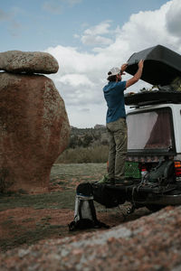 Full length of hiker standing on car trunk against rock formation