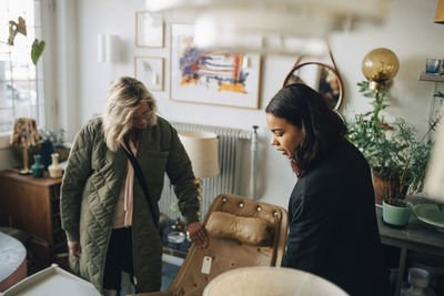 High angle view of female store owner assisting customer buying furniture at antique store
