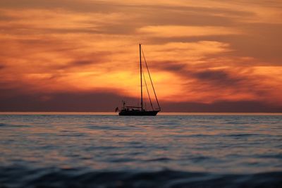 Sailboat sailing on sea against orange sky