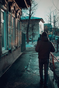 Rear view of man walking on footpath amidst buildings