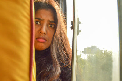 Portrait of young woman looking through window