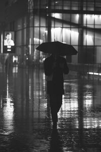 Man walking with umbrella on footpath in rain at night