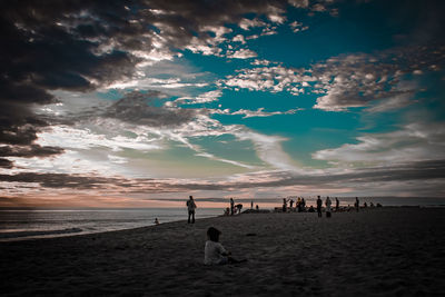 People on beach against sky during sunset