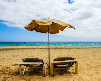 Deck chairs with parasol at beach against sky