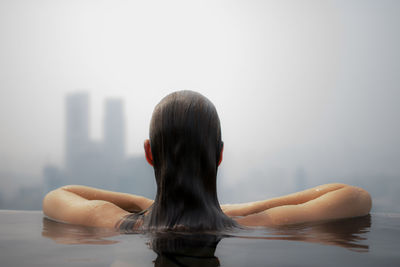 Rear view of woman in infinity pool against skyscrapers