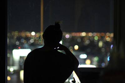 Rear view of silhouette man looking at illuminated city