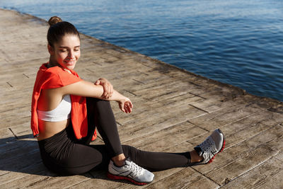 Full length portrait of woman sitting by water