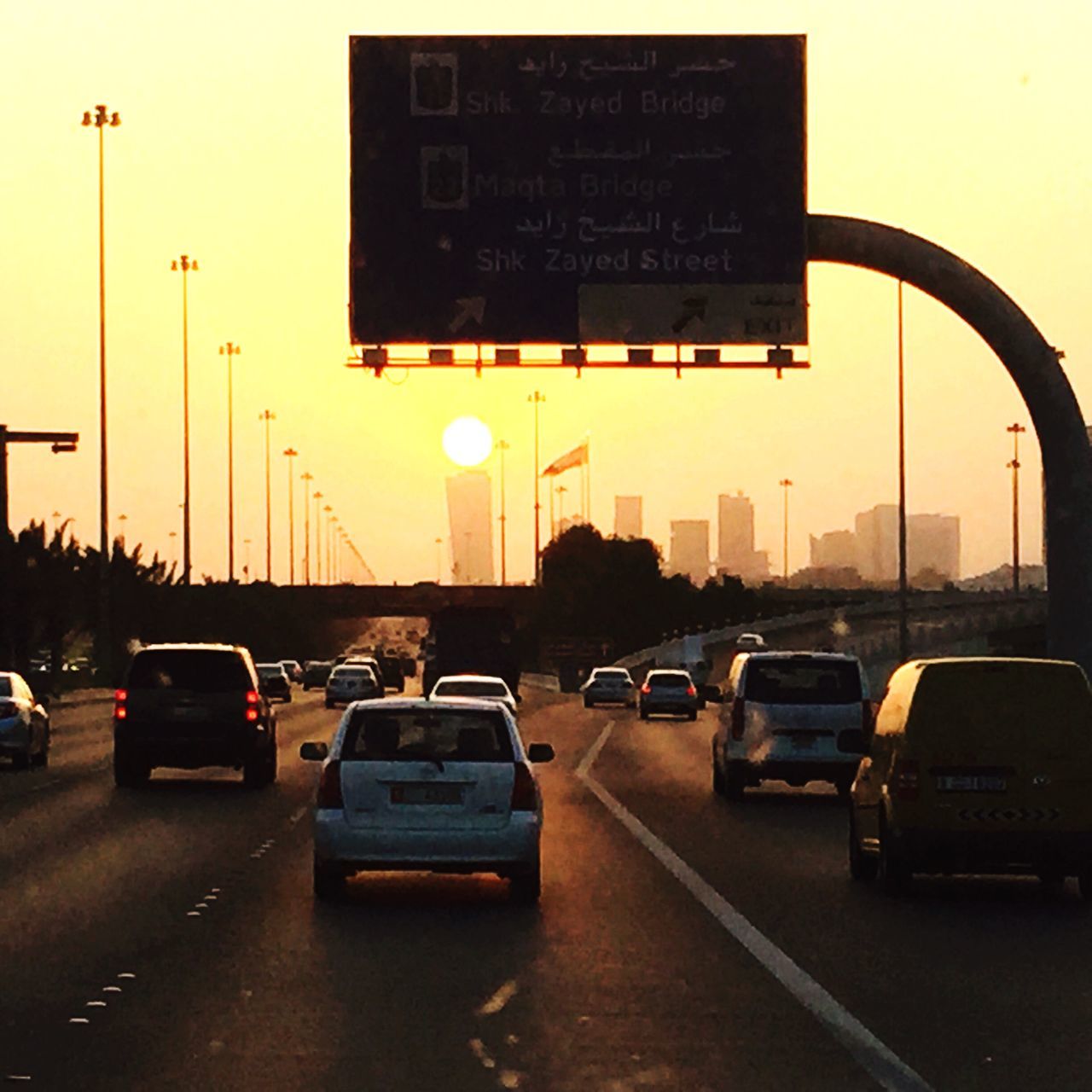 transportation, car, land vehicle, mode of transport, road, street, traffic, street light, on the move, communication, road marking, road sign, city, sunset, sky, the way forward, city street, text, architecture, built structure