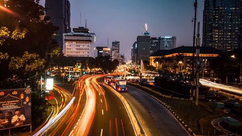 Light trails on road amidst buildings against sky at night