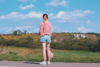 Rear view of young woman standing on land against sky